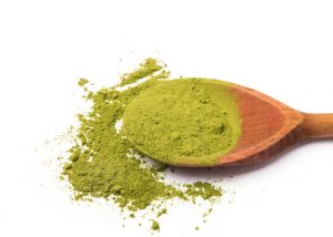 matcha green tea powder on a wooden spoon spilling over onto a white tabletop