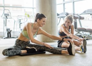 two women in stylish workout gear stretching at the gym