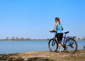 woman with her bicycle at a water's edge looking out onto the lake