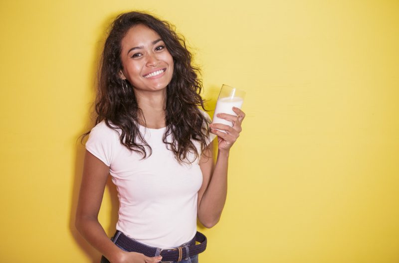 Smiling woman holding up a glass of milk against a yellow backdrop