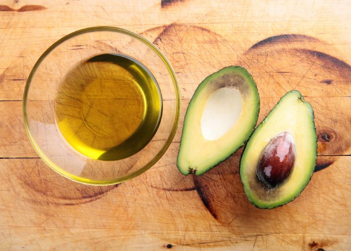 a small clear dish of avocado oil and two halves of a whole avocado beside it