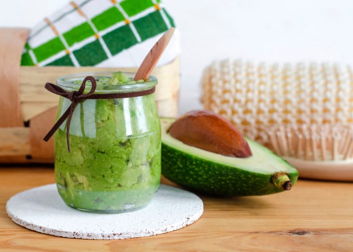 a fresh jar of DIY homemade avocado face mask, with wooden spa brush and towels behind