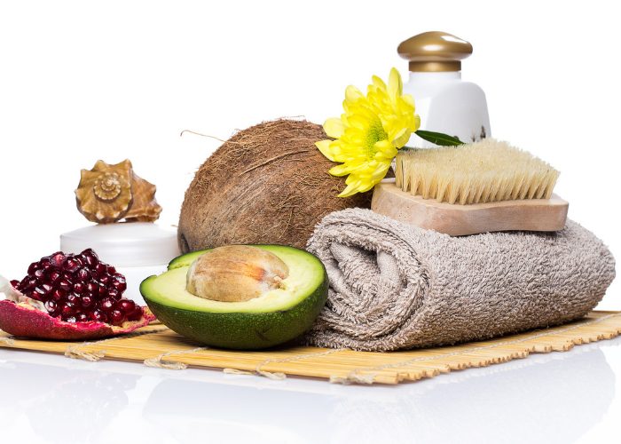 spa ingredients and essentials including avocado oil, coconut, towel, and brush on a table