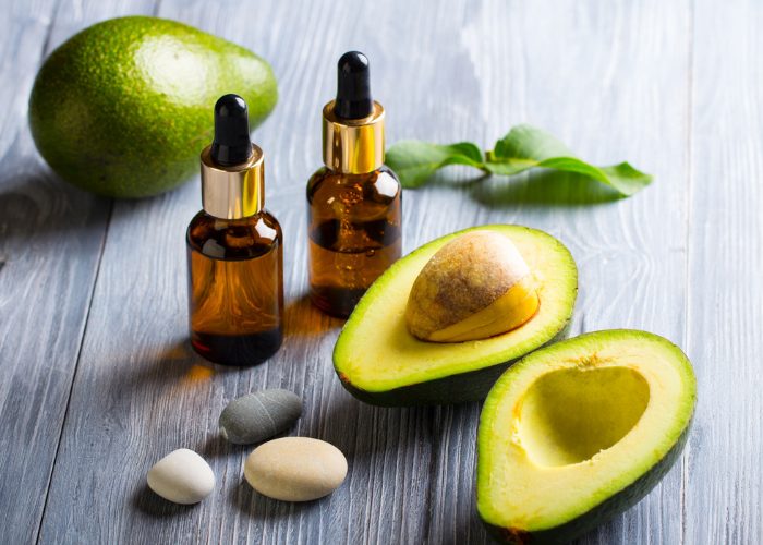 avocado oil in dark vials and fresh avocado being used to improve skin and hair condition