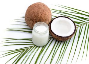 a jar of coconut oil, half a coconut, and a whole fresh coconut laid on a green palm leaf