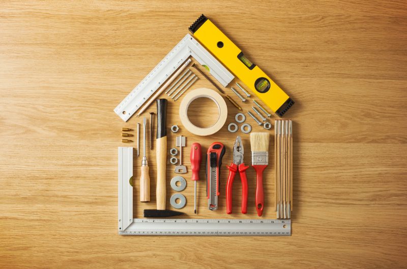 DIY tools such as paint brushes, screwdrivers, rulers etc arranged in the shape of a house