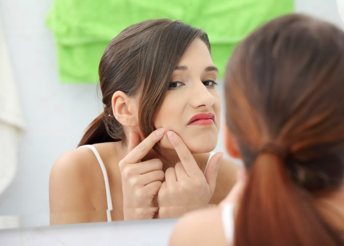 woman squeezing her zit in front of a mirror