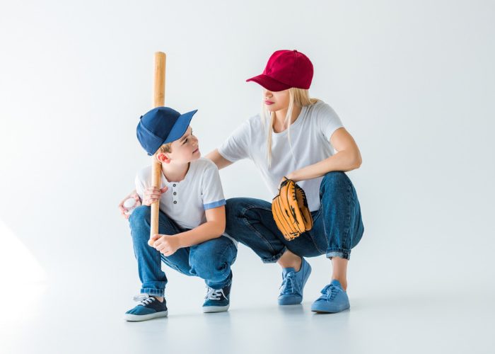 a mother and her son with blue and red baseball caps on holding a baseball bat and glove