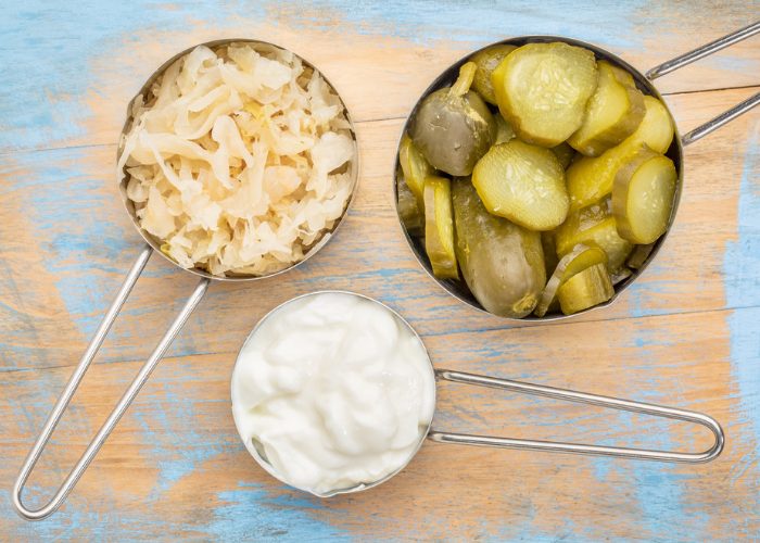 Three bowls of probiotic-rich foods - pickles, sauerkraut, and yogurt on a wooden table