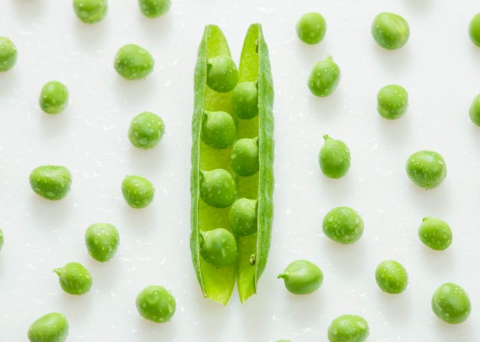 an open pod of peas with other fresh peas scattered around it