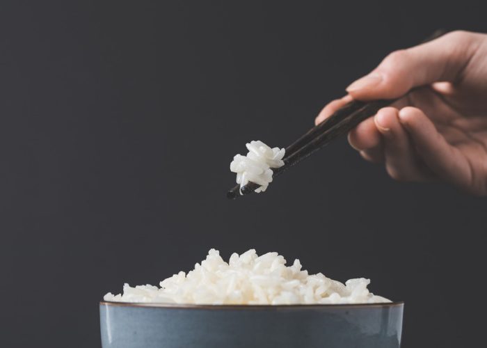 woman picking up a small bunch of glutinous rice with chopsticks over a bowl of rice