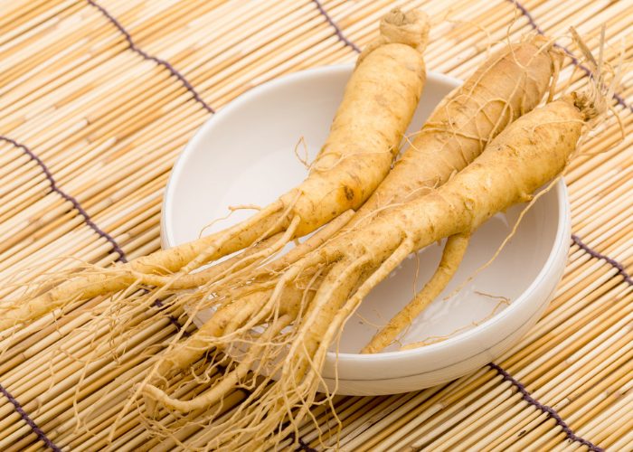3 whole ginseng roots on a white dish on a bamboo mat