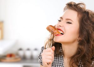 woman biting into a piece of meat on a fork in her kitchen 