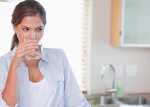 woman drinking a glass of water in her kitchen to stay hydrated