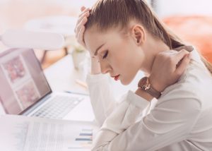 woman at her work desk with eyes closed looking tired