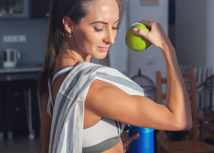 woman holding a green apple and flexing her biceps