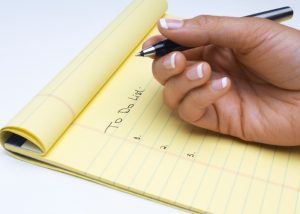 woman holding a black pen with a yellow notepad writing a to do list