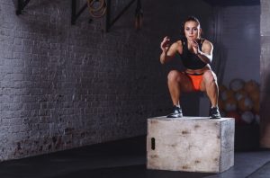 Woman in black top and orange shorts doing box jump plyometric exercises at the gym