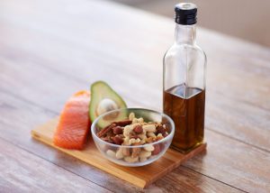 a portion of fresh salmon, half an avocado, nuts in a bowl and olive oil on a wooden board