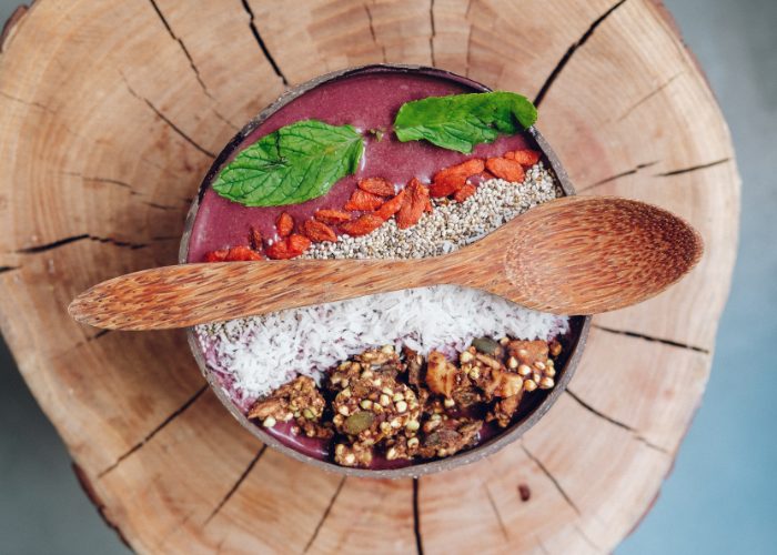 healthy vegan gluten free breakfast bowl including coconut flakes, chia seeds, goji berries, and a nut mix on a wooden base, in a wooden bowl with a wooden spoon