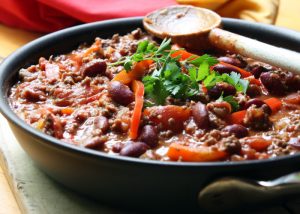 a bowl of soya mince chili con carne with a wooden spoon on the side