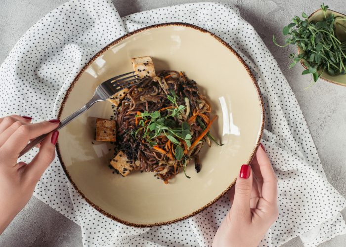 woman holding a fork with a vegan dish of stir fried buckwheat noodles and tofu