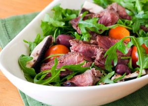 A dish with green salad and roast beef