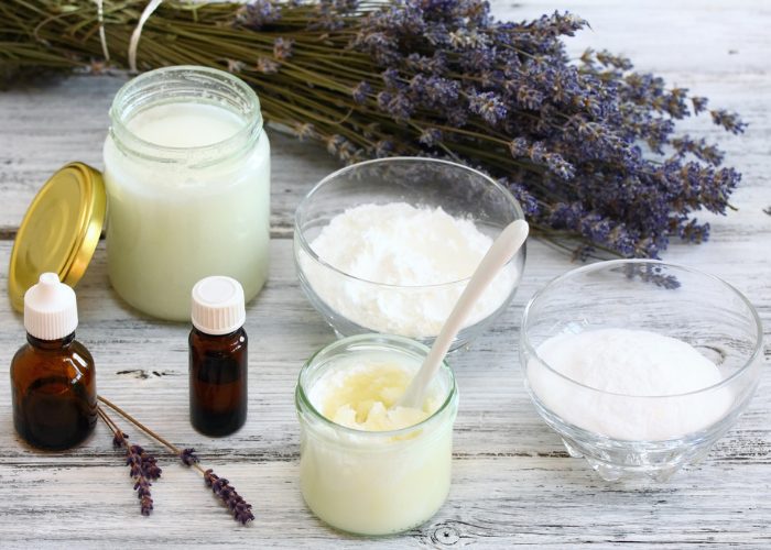 Homemade natural deodorant ingredients in jars and dishes on a wooden table with a bunch of lavender in the background