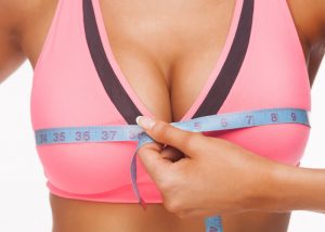 Woman in pink sports bra with a measuring tape measuring her bust size to find the best sports bra for her