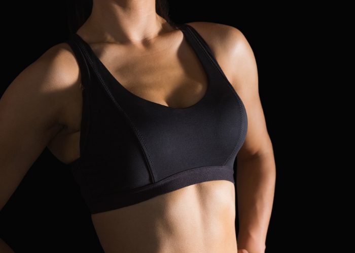 Woman in a plain black sports bra standing against a black background