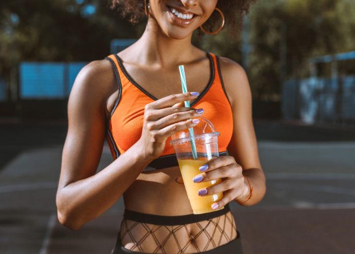 African American woman wearing trendy orange sports bra holding a cup of orange juice