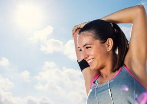 Woman in grey and pink sports bra smiling and doing arm stretches