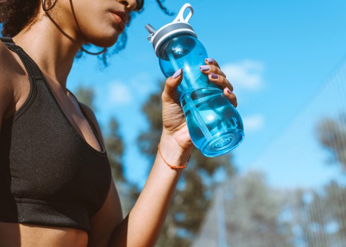 Woman in black sports bra drinking from a blue water bottle outdoors