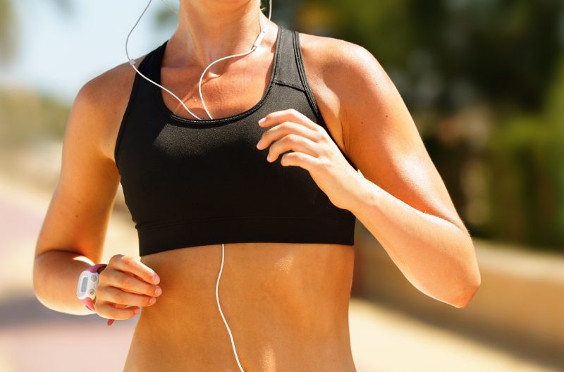 Woman jogging outdoors in black sports bra and with earphones