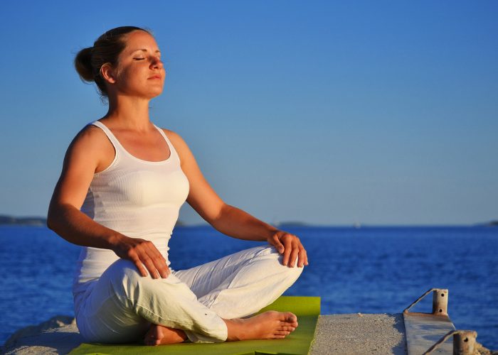 Woman sitting outdoors by the sea on a green yoga mat doing breathing exercises