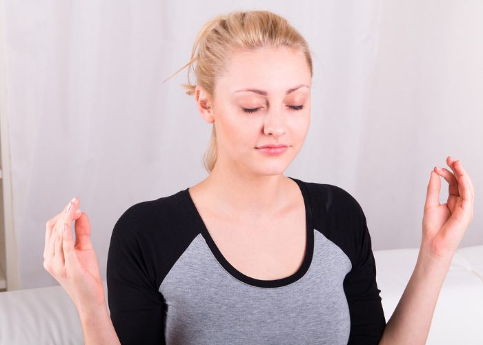 Blonde woman with eyes closed with hands in mudra doing breathing exercises