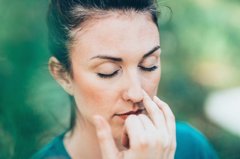 Woman with eyes closed and finger next to her nose doing breathing exercises