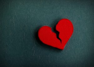Cut out shape of a red broken heart against a dark grey background