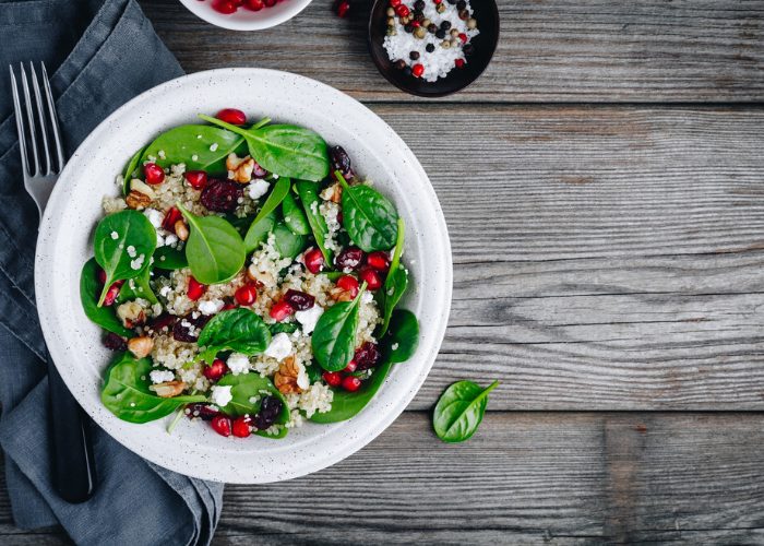 Plant-based Buddha bowl with spinach, grains, pomegranate seeds, set on a wooden table