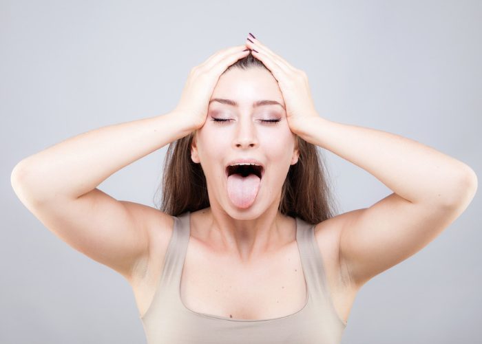 Woman doing face yoga with her eyes closed and face open wide with tongue sticking out