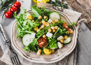 Plate of green salad with cucumbers, greens, tomatoes, and chickpeas on a beautiful grey plate on grey tablecloths