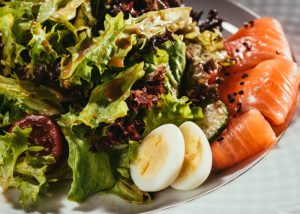 Flexitarian plate of salad greens and dressing, with a few pieces of salmon and two halves of a quail egg