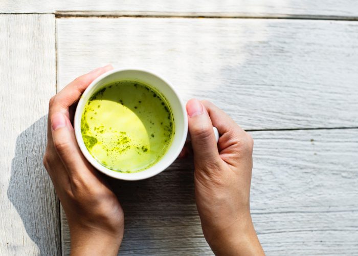 Top-down view of woman holding a mug of warm matcha tea.