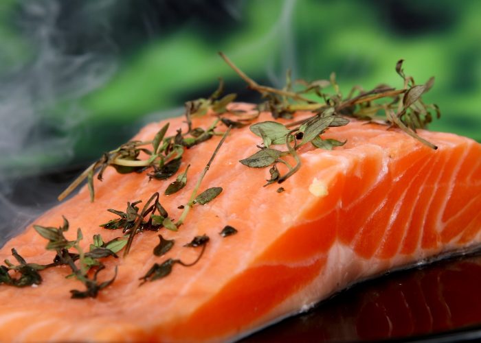 A closeup of raw salmon topped with fresh herbs ready to be put in the oven