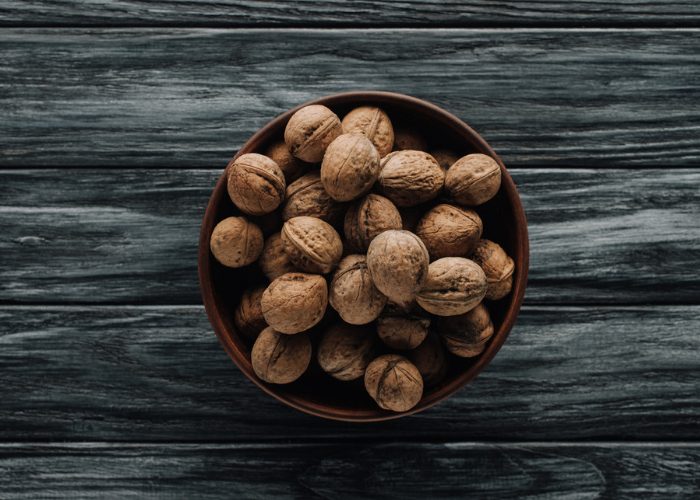 A bowl of whole walnuts on a dark grey wooden table