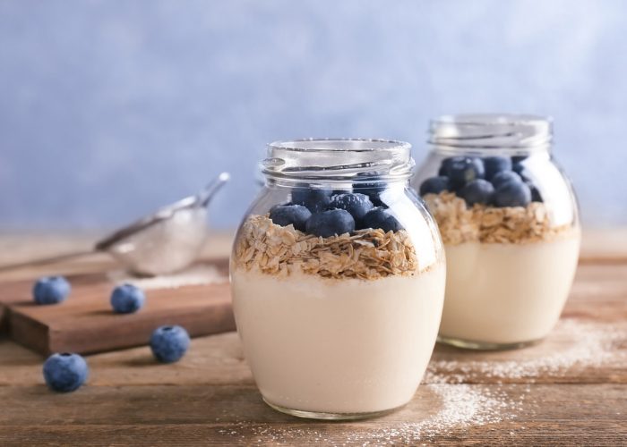 Two jars of yogurt topped with oats and blueberries on a wooden table