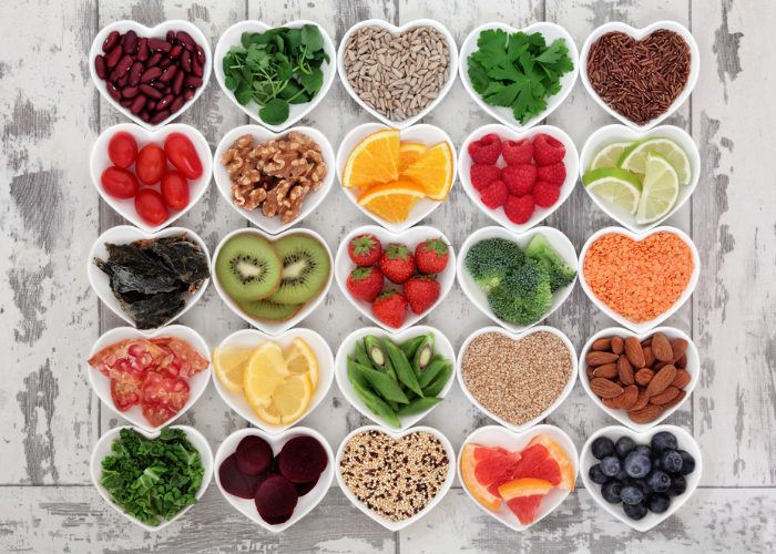 Different healthy foods and vitamins such as fruits, berries, nuts, seeds, and vegetables, in many heart-shaped bowls
