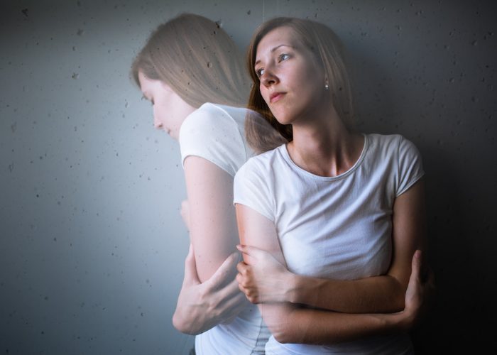 Anxious and depressed woman hugging herself and leaning against a dark wall