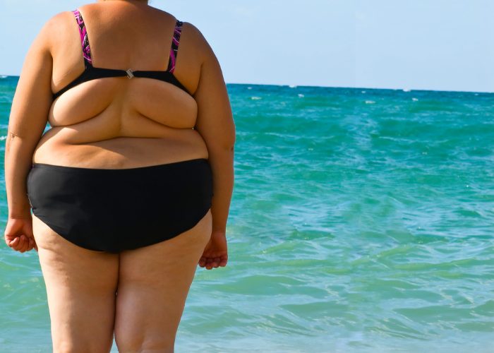Obese woman in a black bathing suit standing by the sea