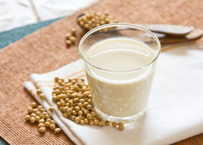 a glass of soy milk on white cloth with soybeans next to it